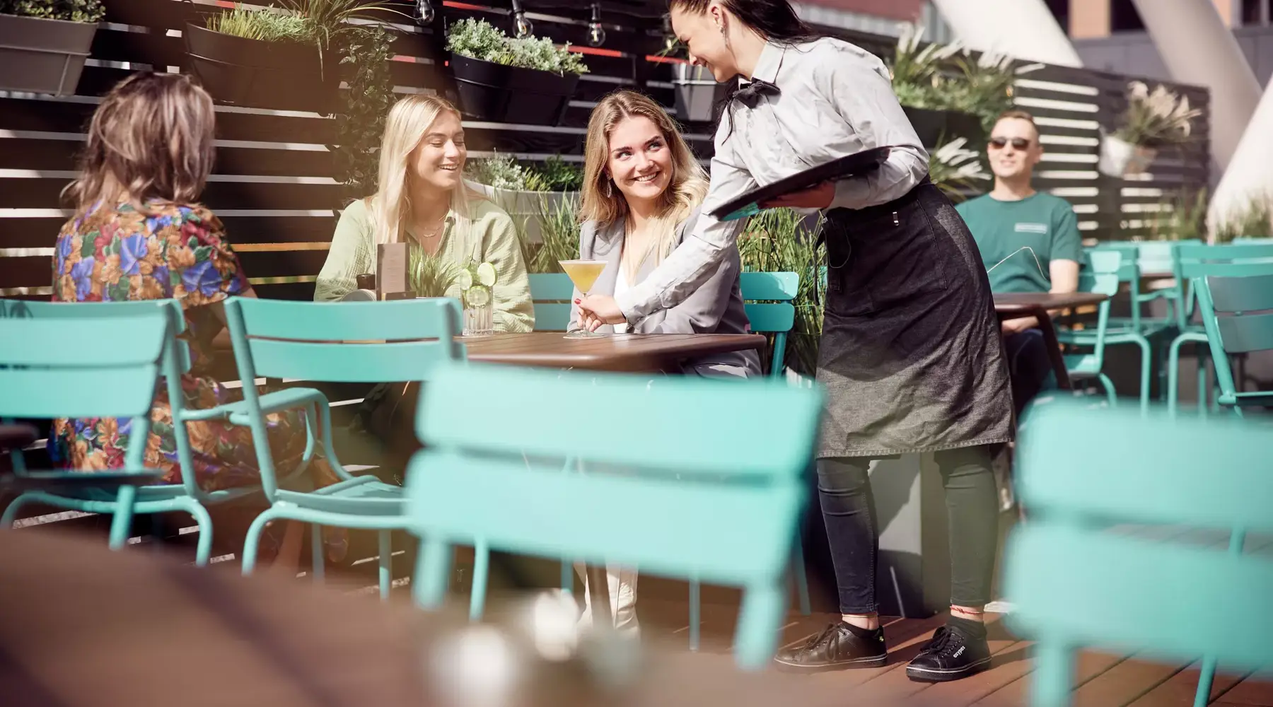 Two women are sitting on a terrace and being served.