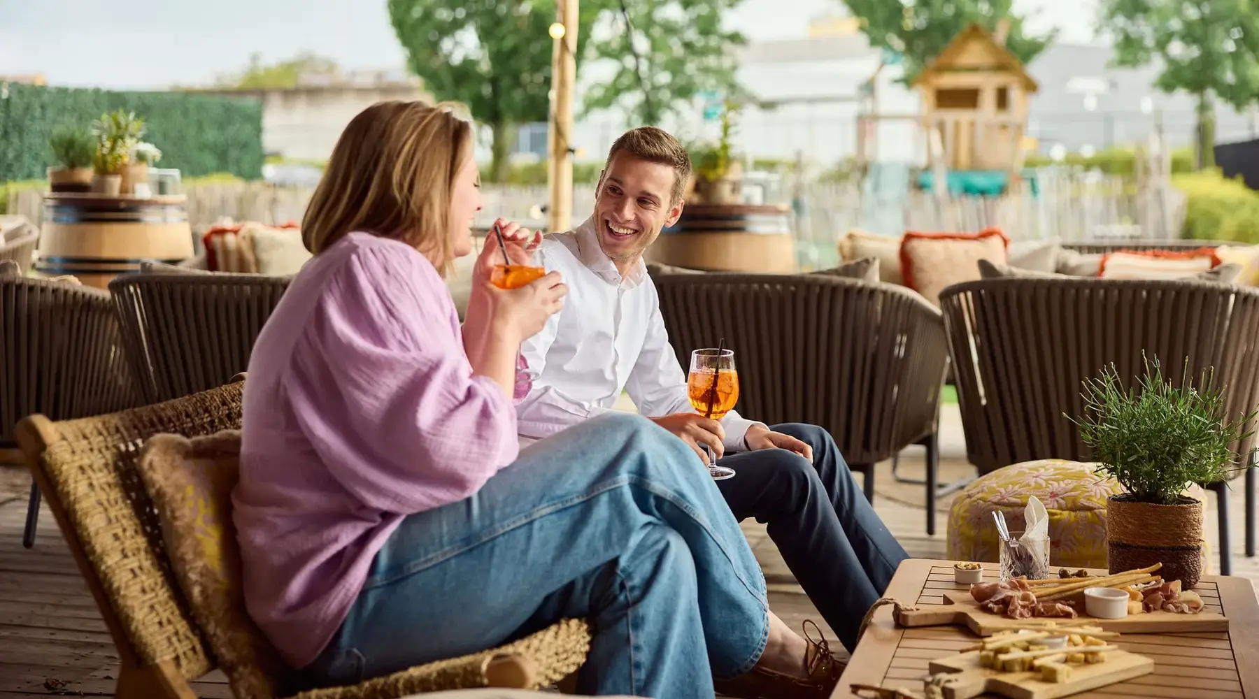 Two people enjoy a drink on a covered terrace.