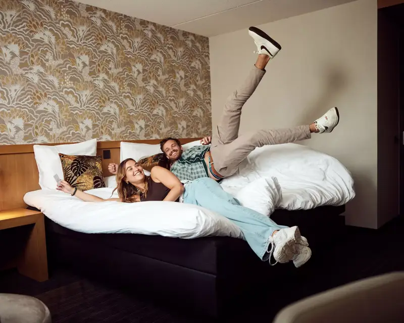 Couple jumps on the bed in a hotel room at Hotel Drachten.