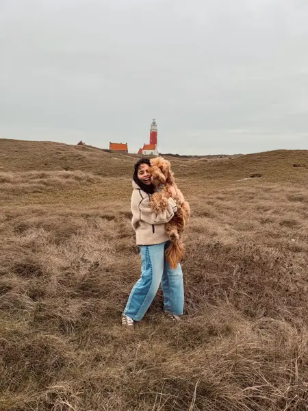 Vrouw knuffelt haar hond in de duinen voor de vuurtoren van Texel