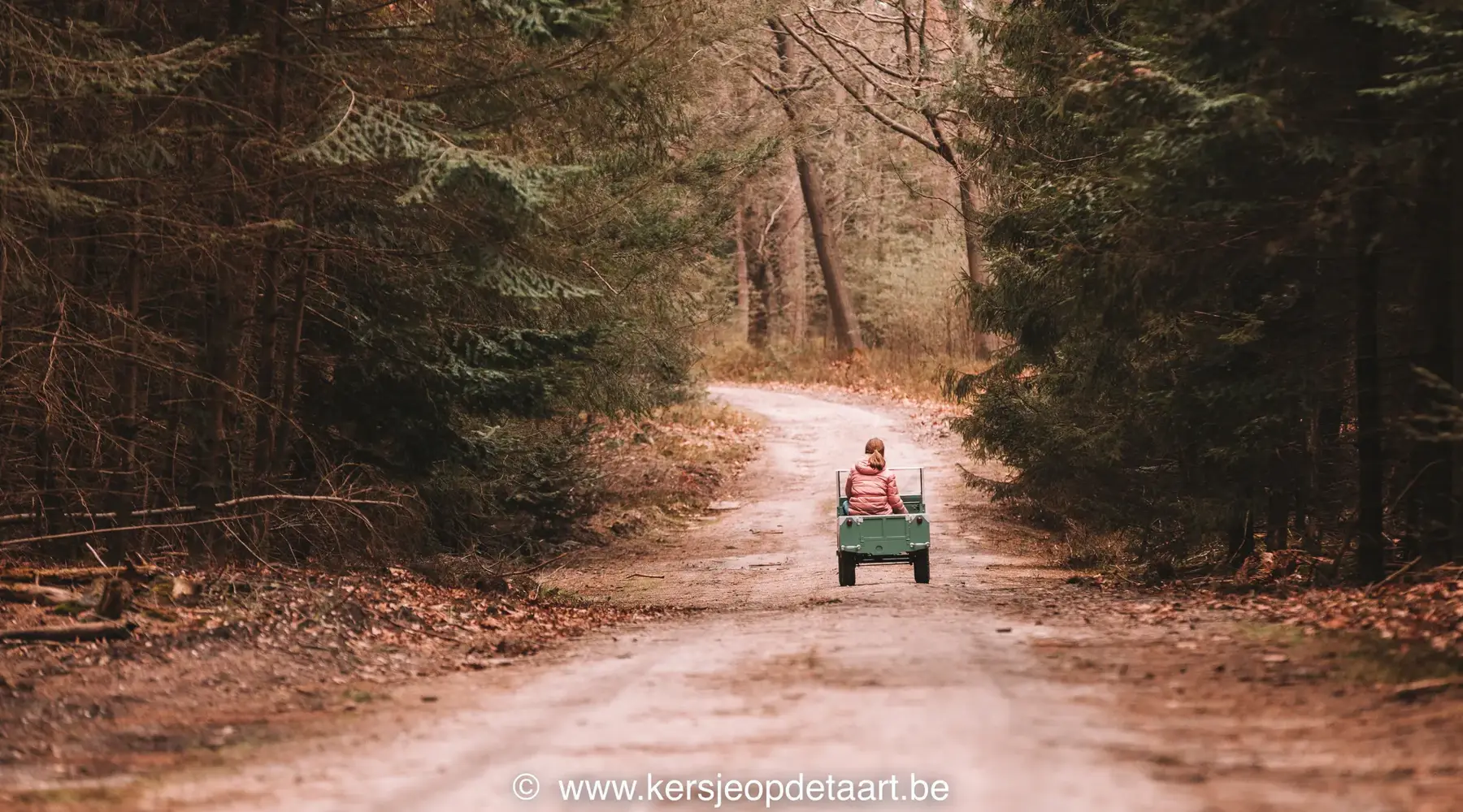 Meisje met roze jas door het bos op een mini landrover