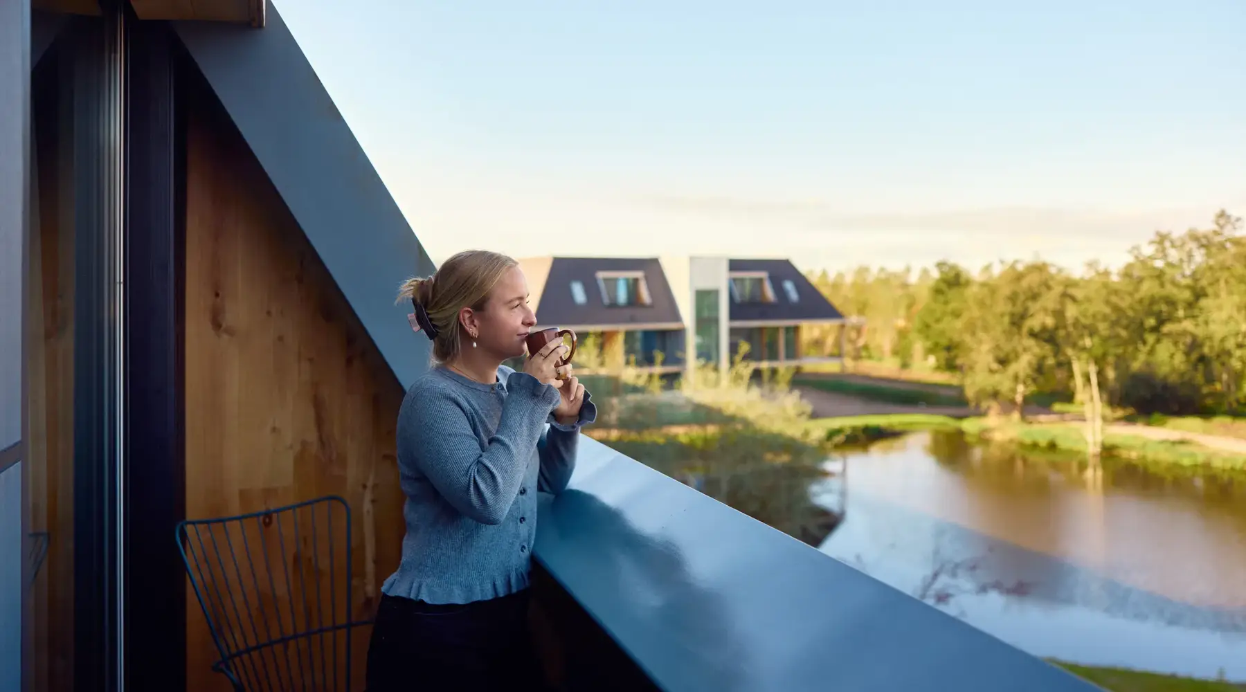 Woman is drinking coffee on her hotel room with balcony.