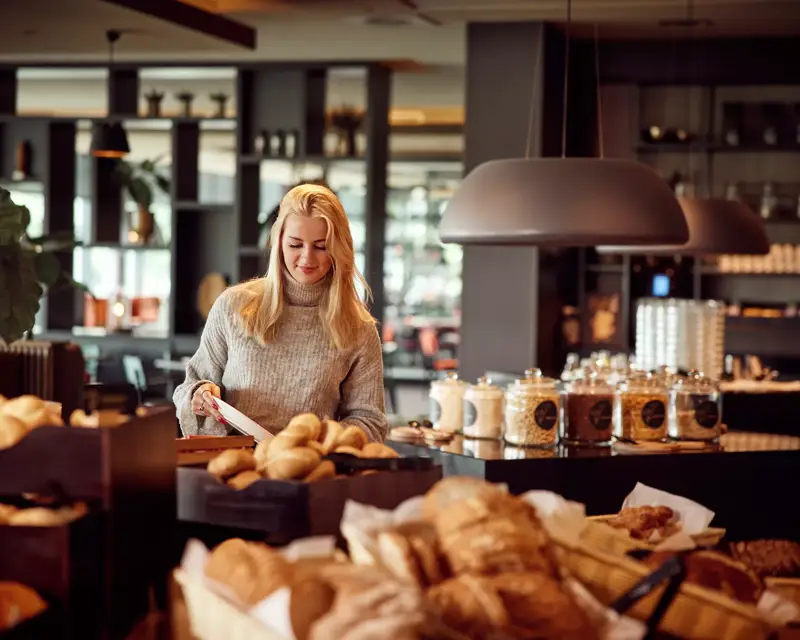 Woman takes a sandwich from the breakfast buffet.