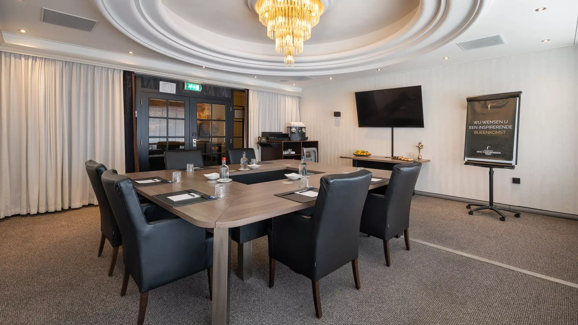 Broad view of the meeting room with the central block layout, presentation facilities, and the private coffee and beverage buffet in the background.