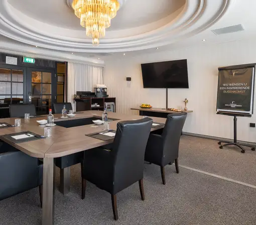 Broad view of the meeting room with the central block layout, presentation facilities, and the private coffee and beverage buffet in the background.