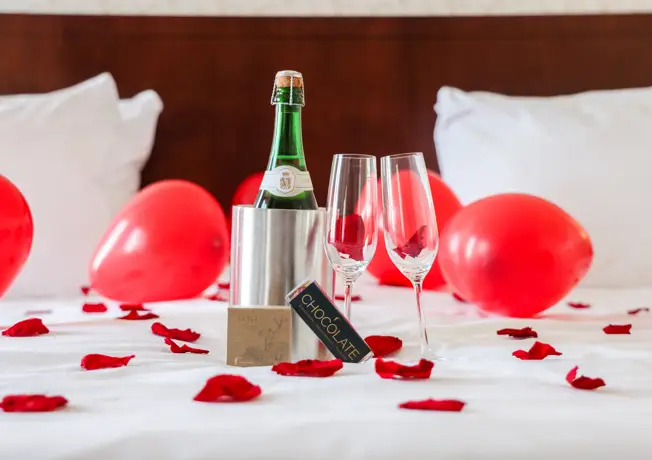 room package with bottle of champagne, rose petals, champagne glasses, chocolate and a bath bomb