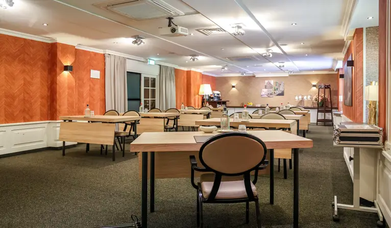 Vue d'ensemble de la salle De Uilenburg avec une disposition des sièges de type scolaire, donnant sur les tables et le buffet de café privé situé au fond de la salle.