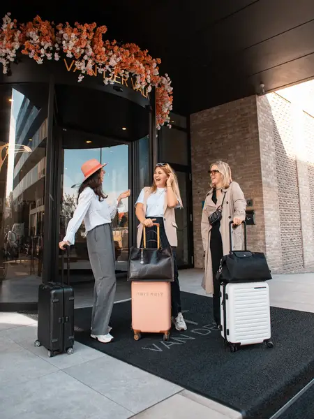 Girlfriends standing with suitcases at the entrance of a Van der Valk hotel