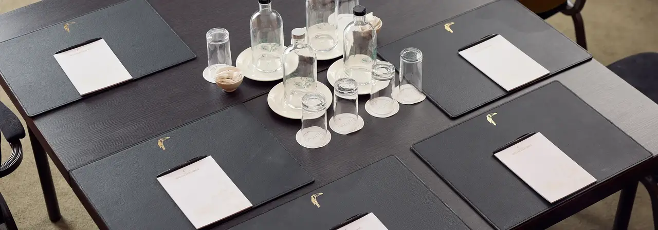 Decken Sie den Tisch für ein Meeting mit Notizblock, Stift, Platzset, stillem und kohlensäurehaltigem Wasser, Gläsern und Pfefferminzbonbons.
