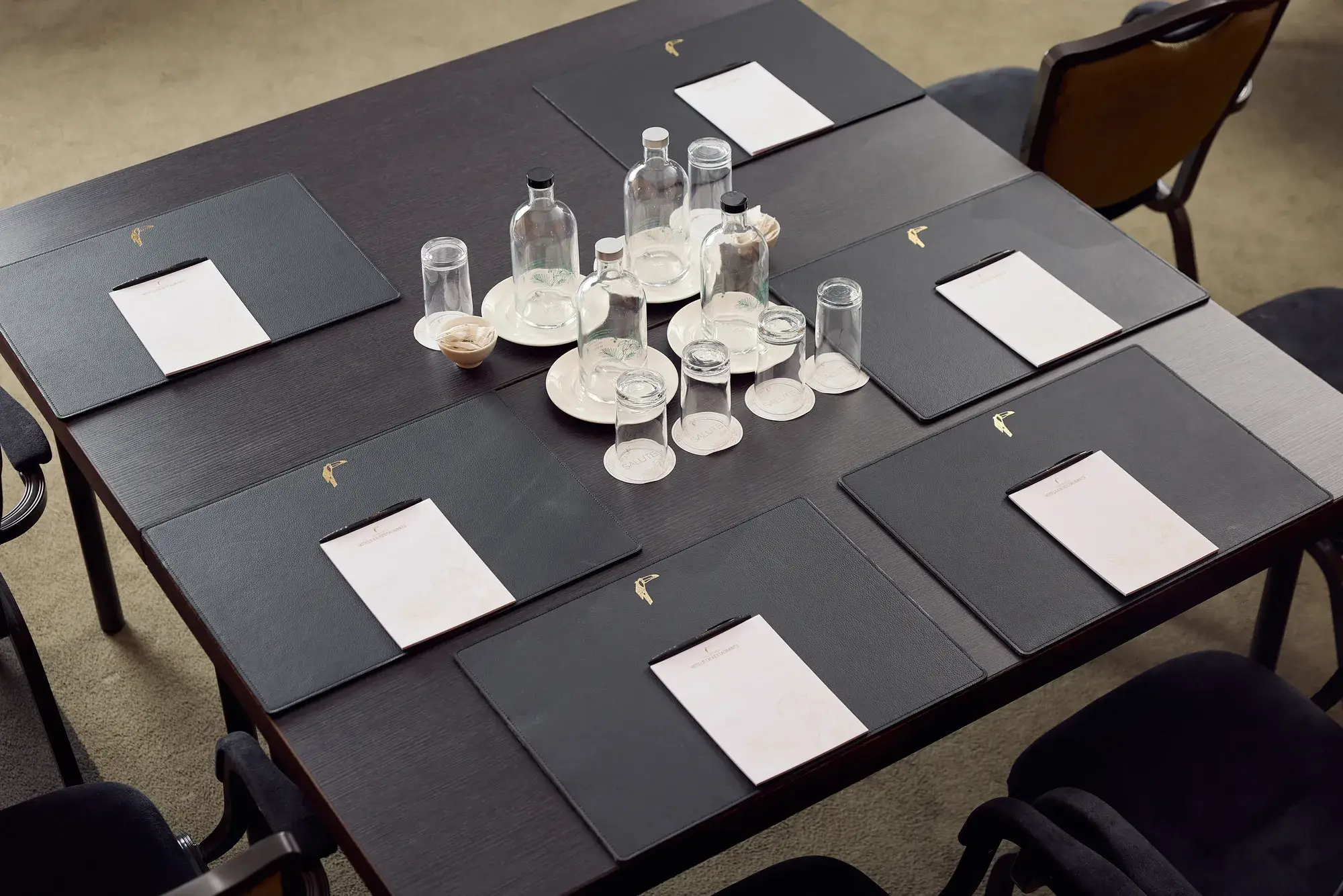 Decken Sie den Tisch für ein Meeting mit Notizblock, Stift, Platzset, stillem und kohlensäurehaltigem Wasser, Gläsern und Pfefferminzbonbons.