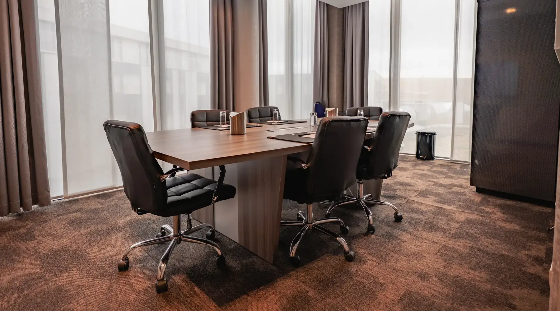 Besprechungszimmer des Hotels Mons mit schwarzen Stühlen und Gläsern auf dem Tisch