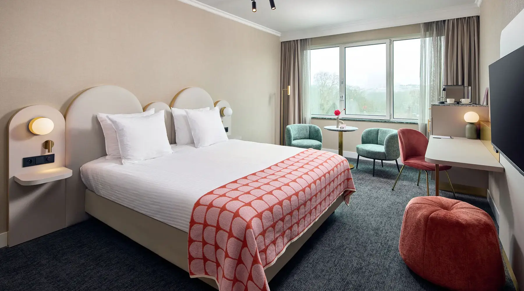 Kamer in het hotel. Voorzien van een twee persoons bed 3 stoelen en een rode poef.