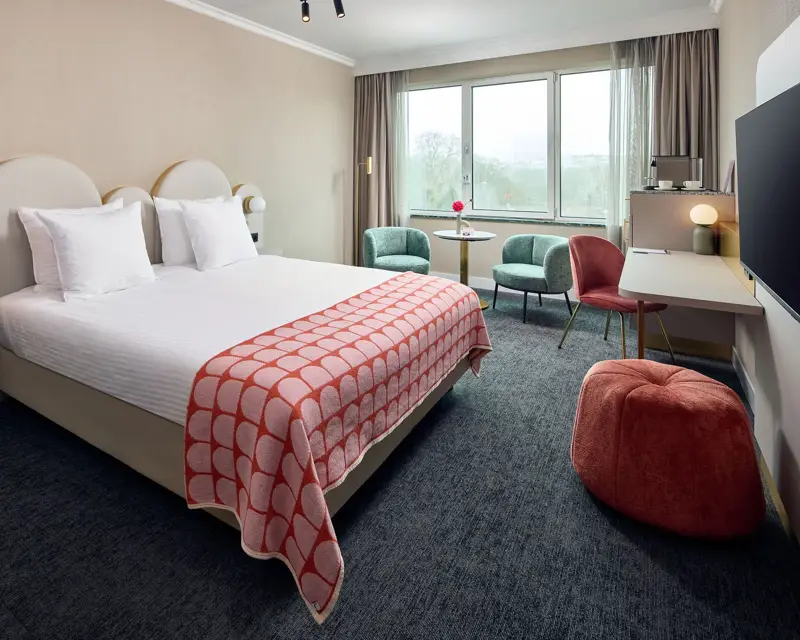 Kamer in het hotel. Voorzien van een twee persoons bed 3 stoelen en een rode poef.