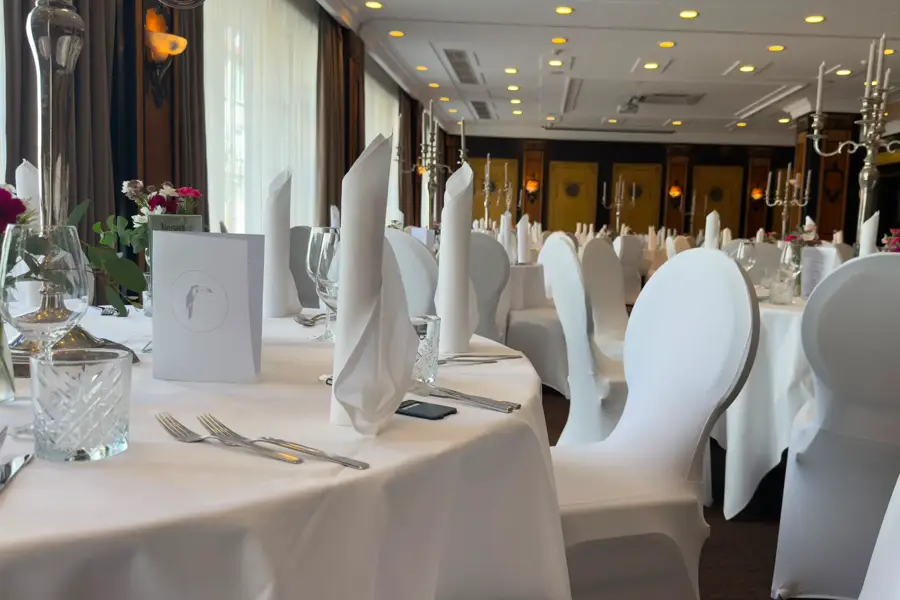Festively set tables with white chair covers, cloth napkins and glasses in the Wollenweber event room of the Van der Valk Hotel Hildesheim.