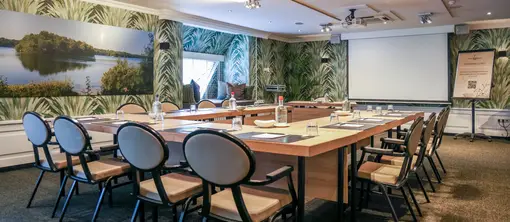 Overview of the De IJzeren Man hall in a U-arrangement, with striking botanical wallpaper and its own coffee buffet with drinks fridge in the background.
