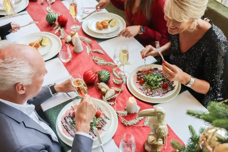 Een gezelschap geniet samen van een culinair kerstdiner aan een feestelijk gedekte tafel met kerstdecoraties.