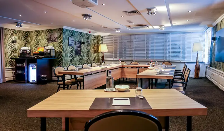 Overview of the De IJzeren Man hall in a U-arrangement, with striking botanical wallpaper and its own coffee buffet with drinks fridge in the background.