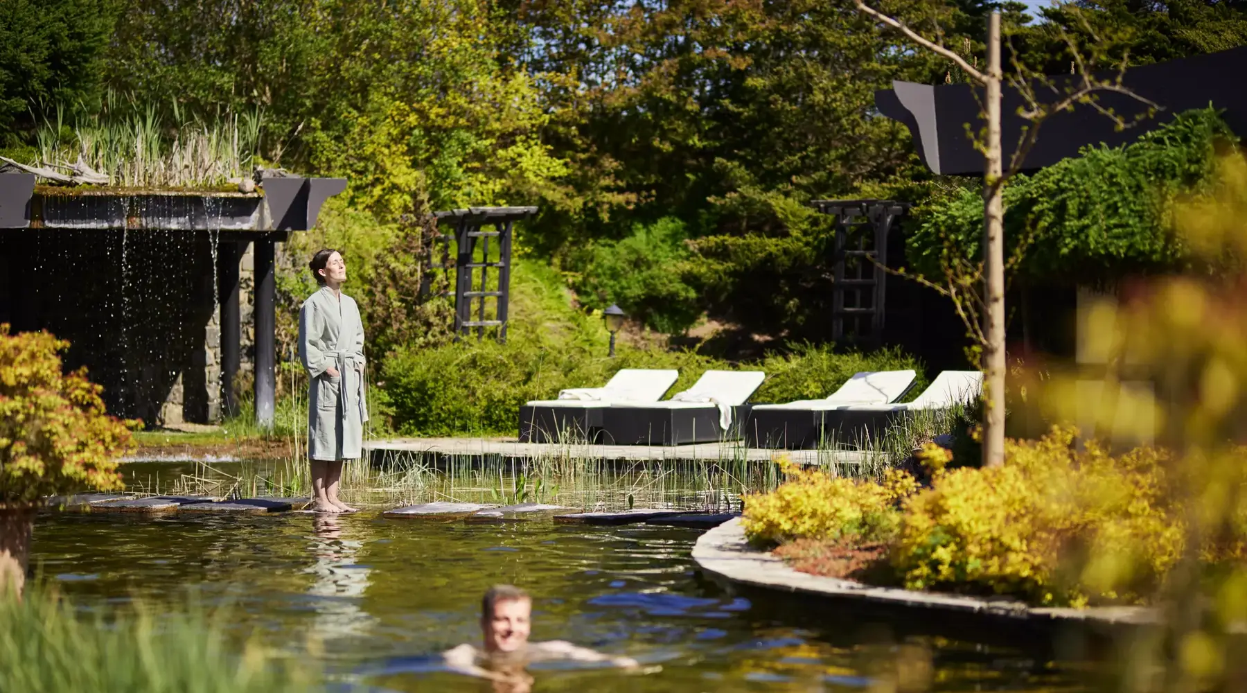 Gäste entspannen am Natur-Schwimmteich mit Liegestühlen im Van der Valk Resort Linstow.