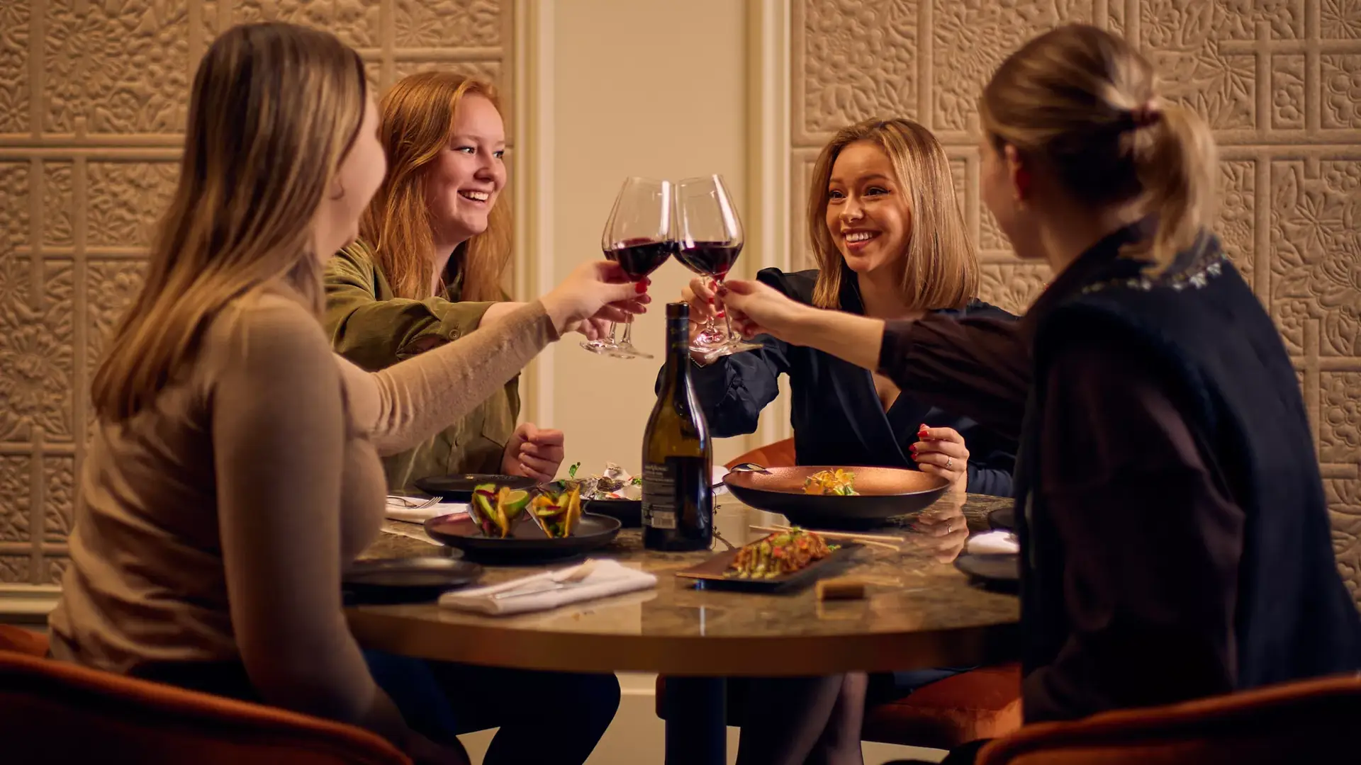 Gruppe von Mädchen prostet sich am Tisch mit Rotwein zu.