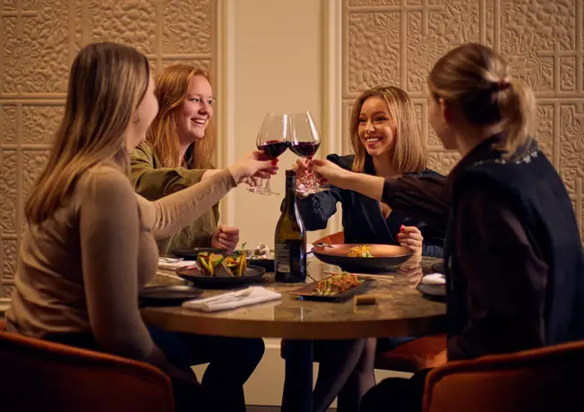 Groep meiden proost aan tafel met rode wijn