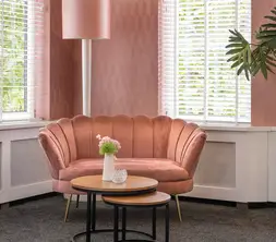 Detail van een comfortabele zithoek in de ruimte, passend ingericht met een roze bankje, tafeltjes en plantendecoratie.