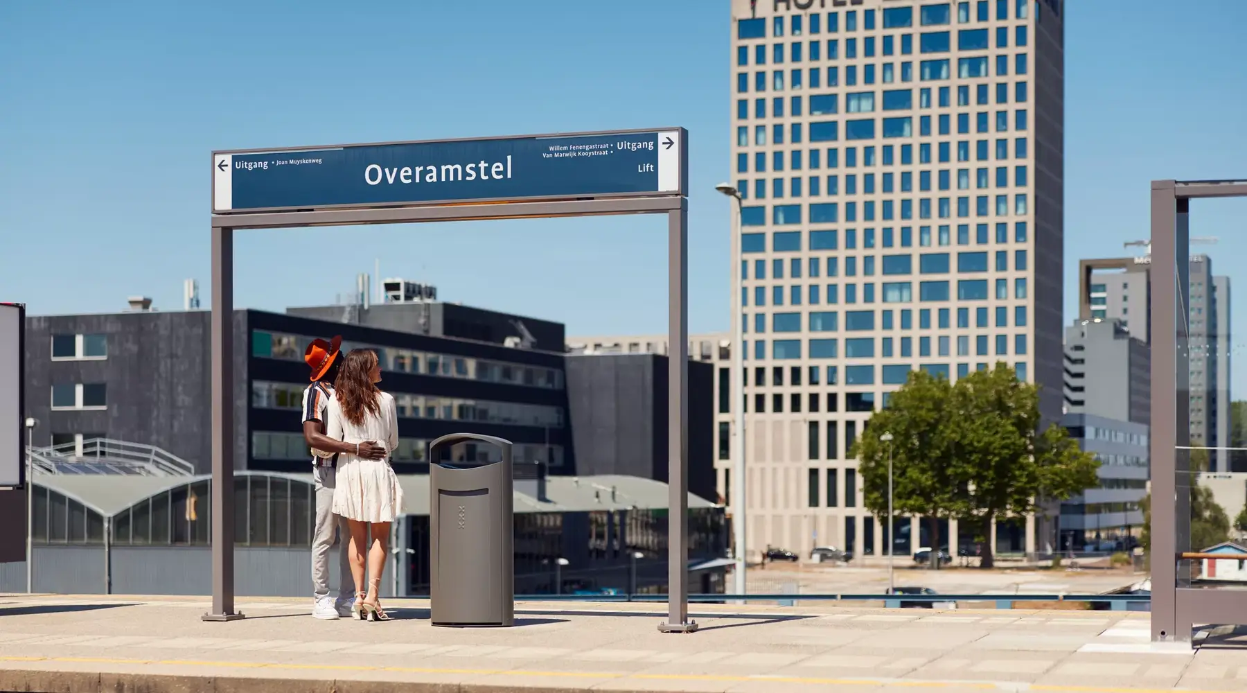Mann und Frau an einer U-Bahn-Station mit Hotel Amsterdam-Amstel im Hintergrund