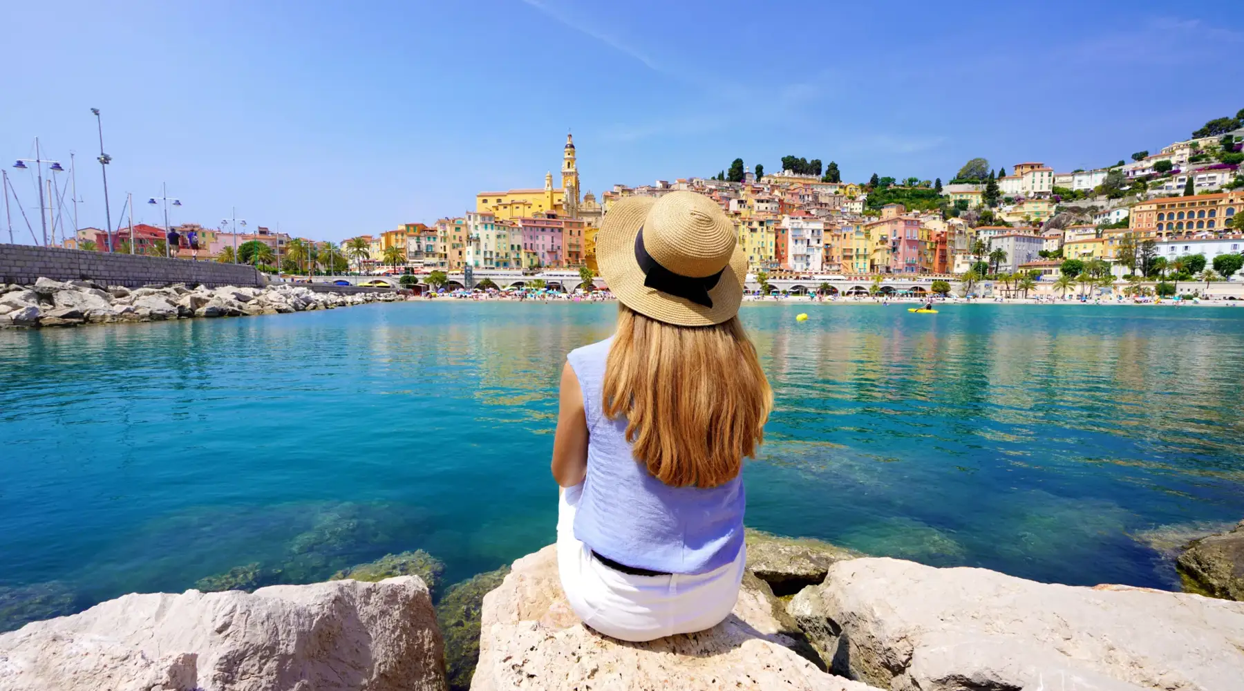 Une dame est assise sur un rocher et regarde la ville de Menton en France.
