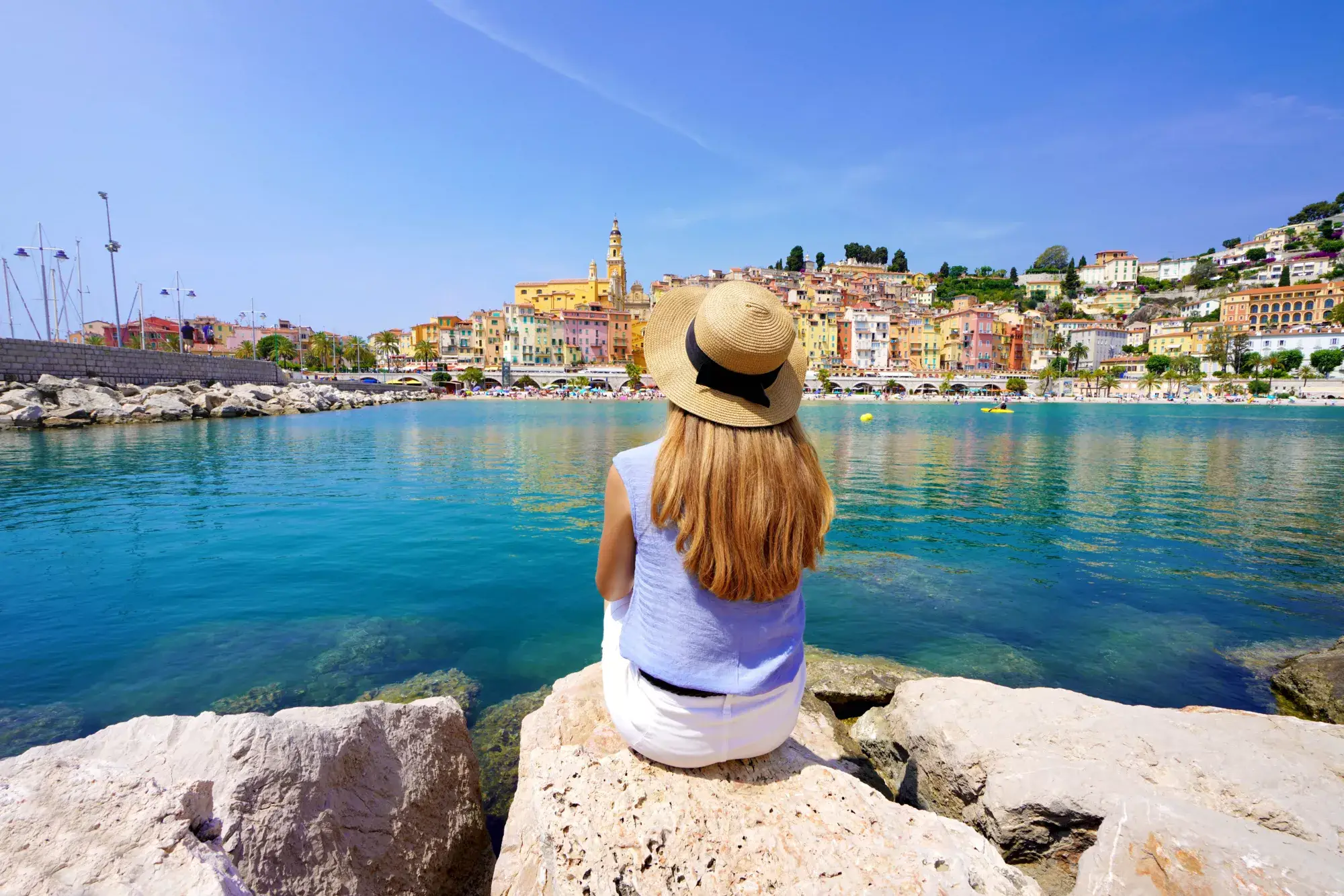 Une dame est assise sur un rocher et regarde la ville de Menton en France.