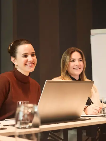 2 vrouwen aan een tafel in pak, met laptop tijdens een vergadering