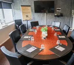 Bovenaanzicht van de ovale vergadertafel in de boardroom, voorzien van geïntegreerde kabelaansluitingen voor presentaties.