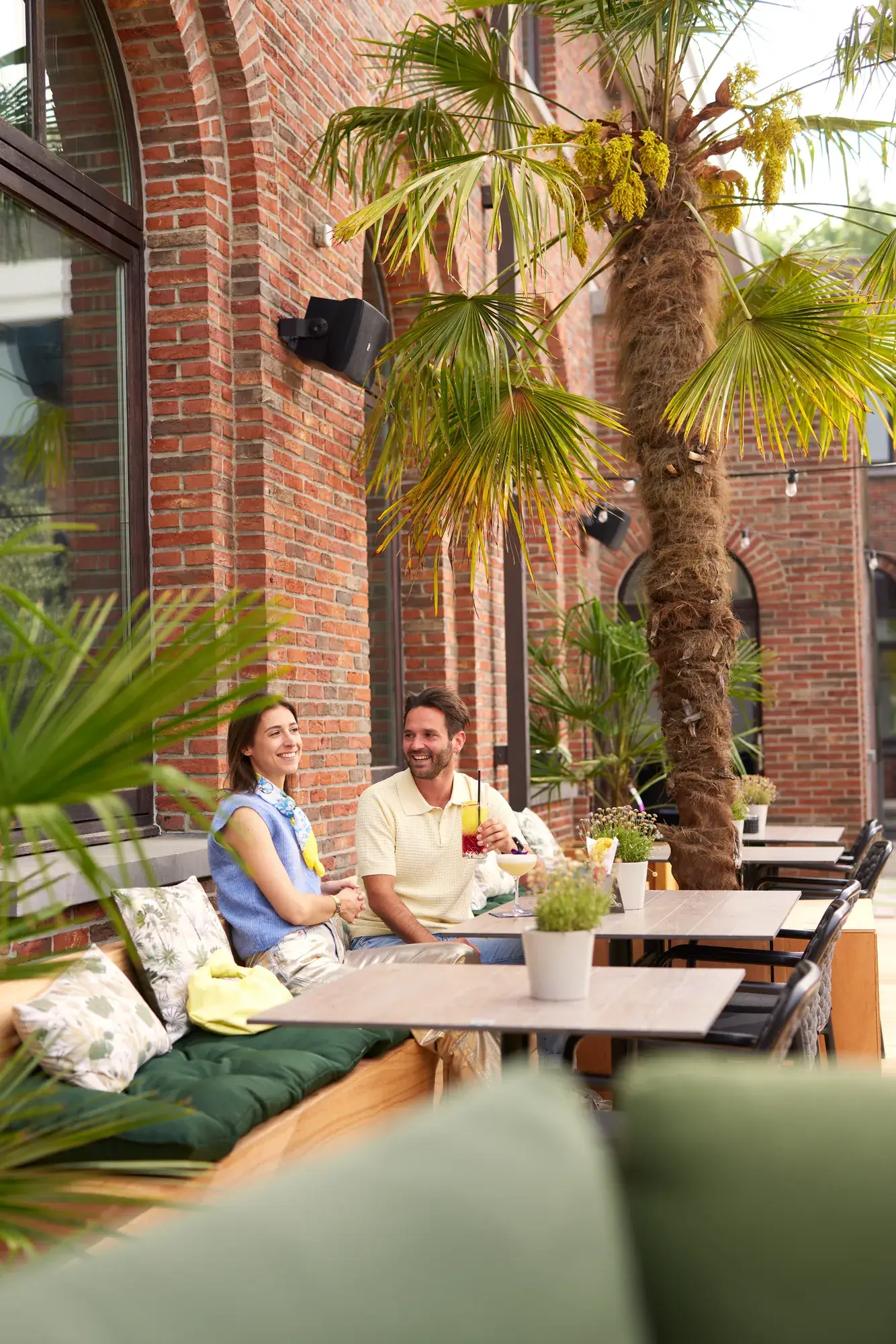 Man en vrouw op het terras van een Van der Valk hotel met drankjes en op de achtergrond palmbomen.