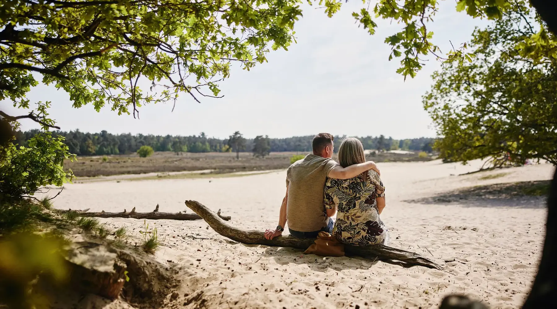 Couple sitting next to each other on a tree trunk on a sandy plain