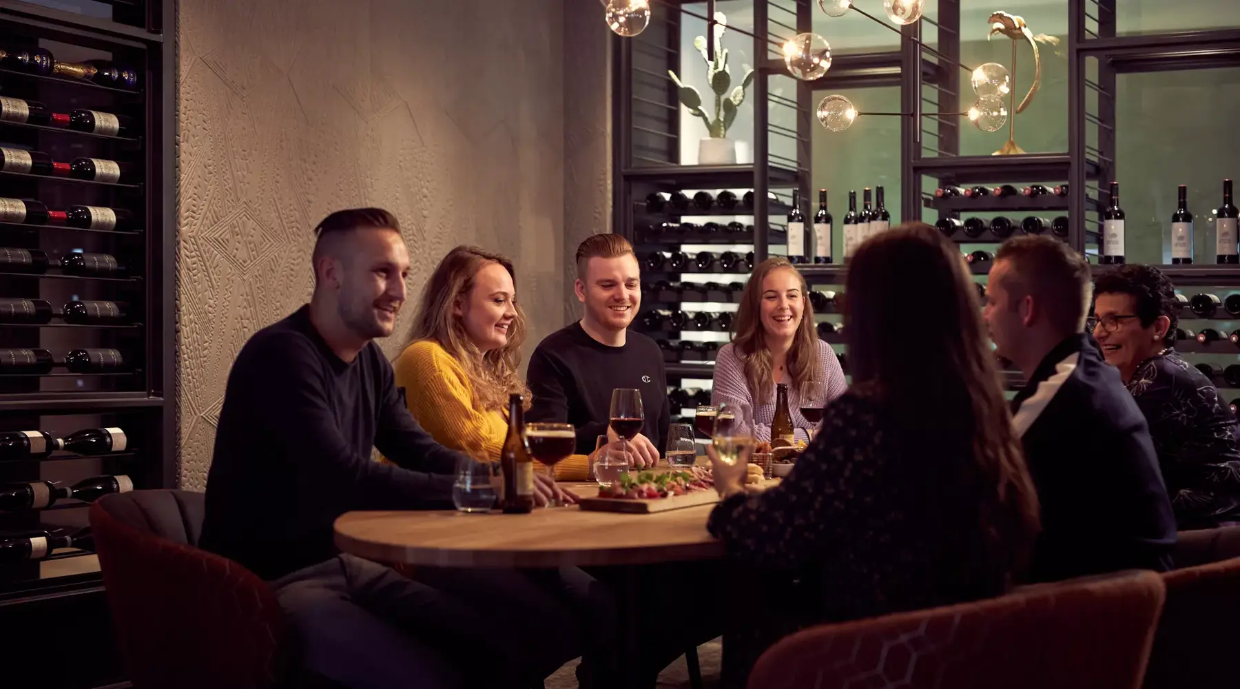 Groep mensen zit gezellig aan tafel met lekker eten en een drankje.