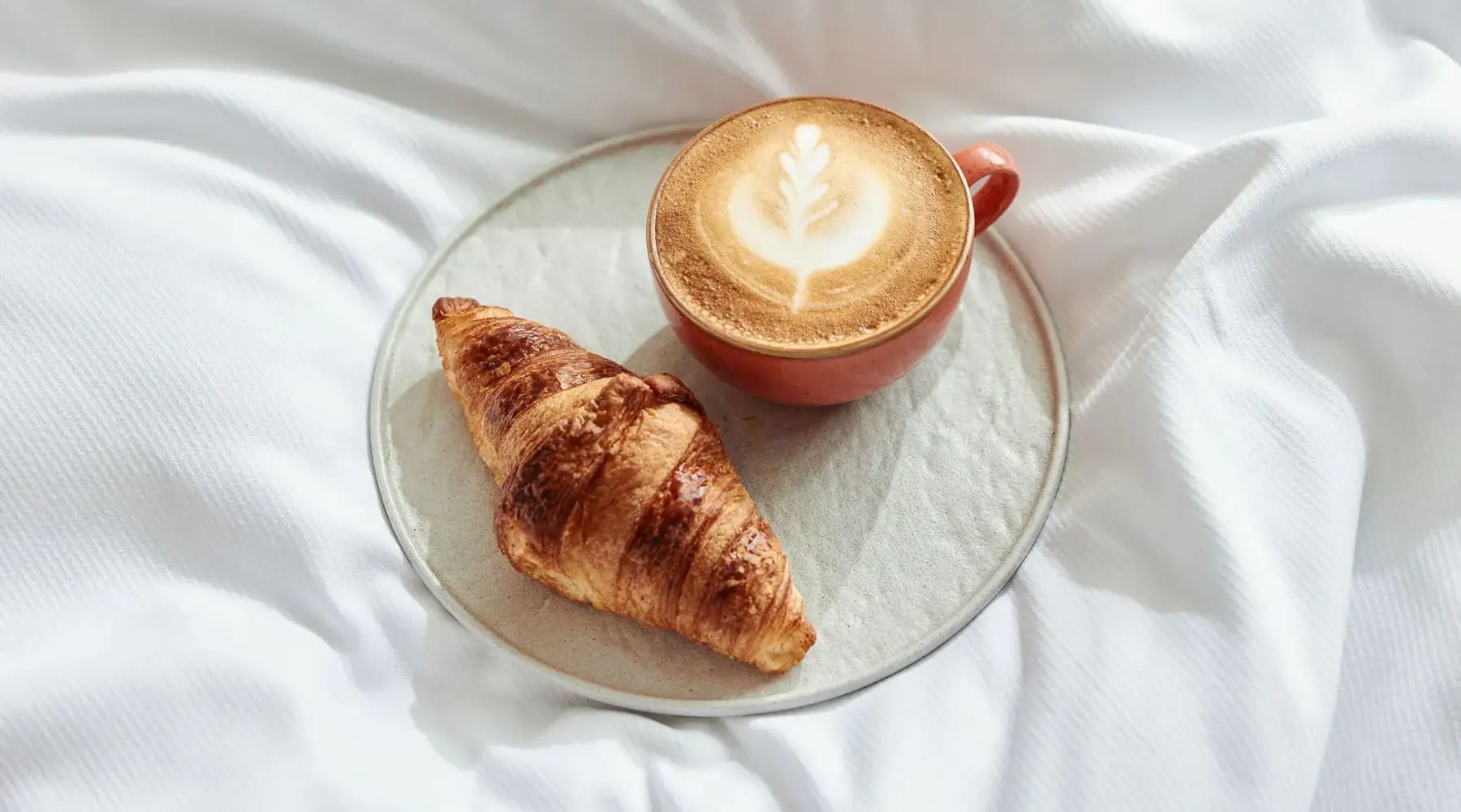 Woman reads newspaper with breakfast in bed.