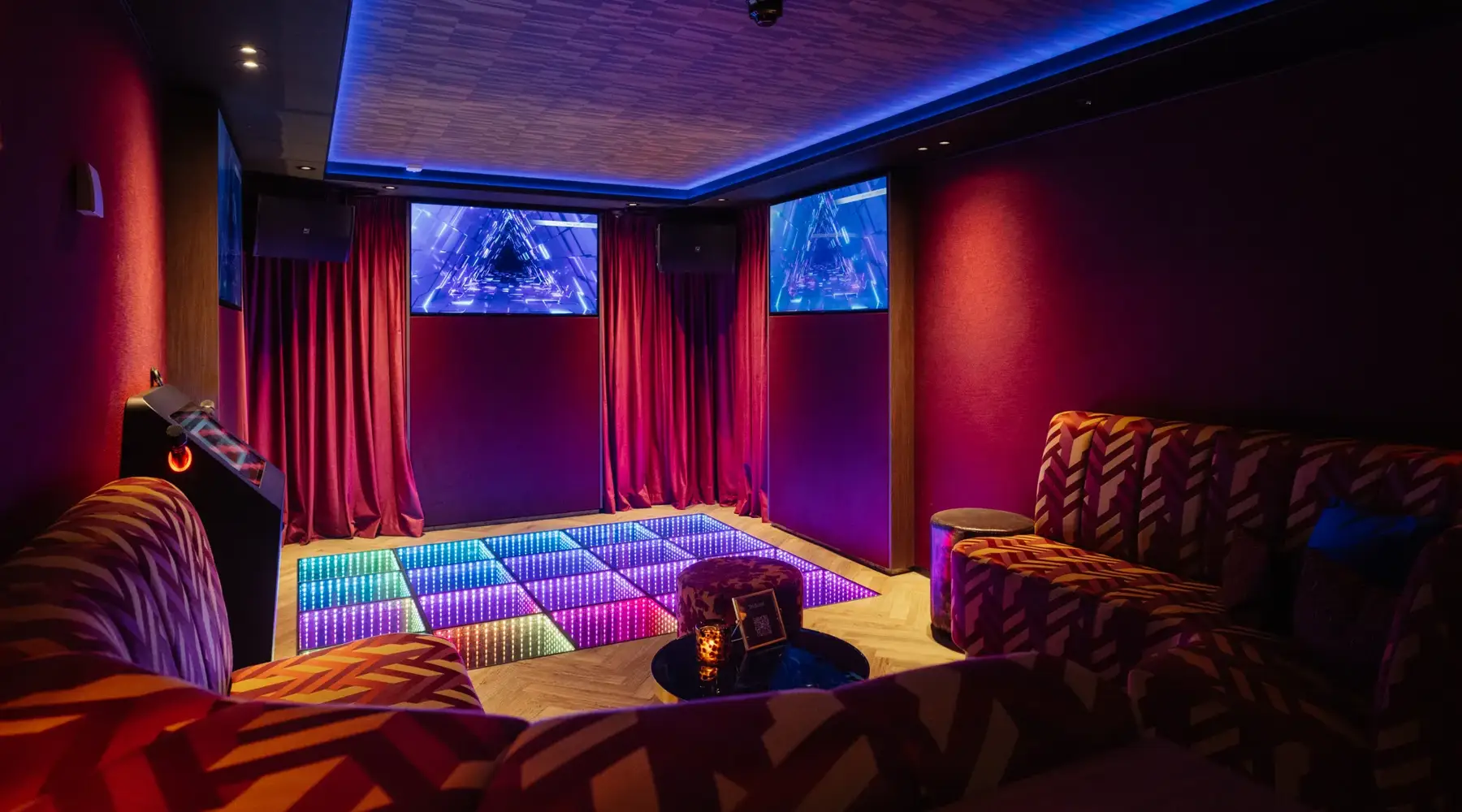 Karaoke lounge with 3 screens and colorful couch.
