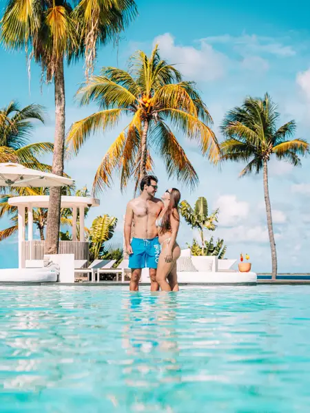 Man en vrouw in zwemkleding aan de rand van een zwembad op Bonaire en omring met palbomen