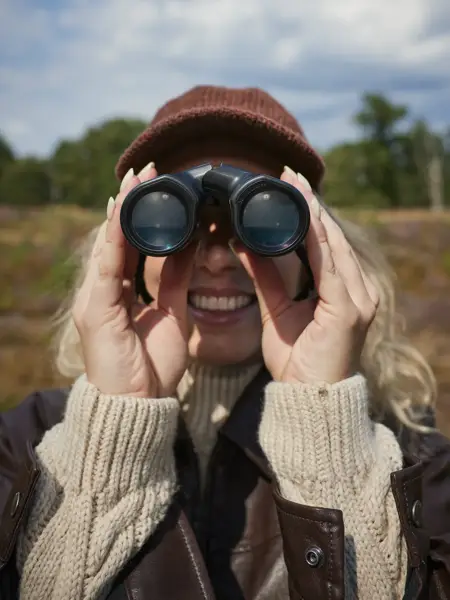 Vrouw kijkt door verrekijker naar de camera