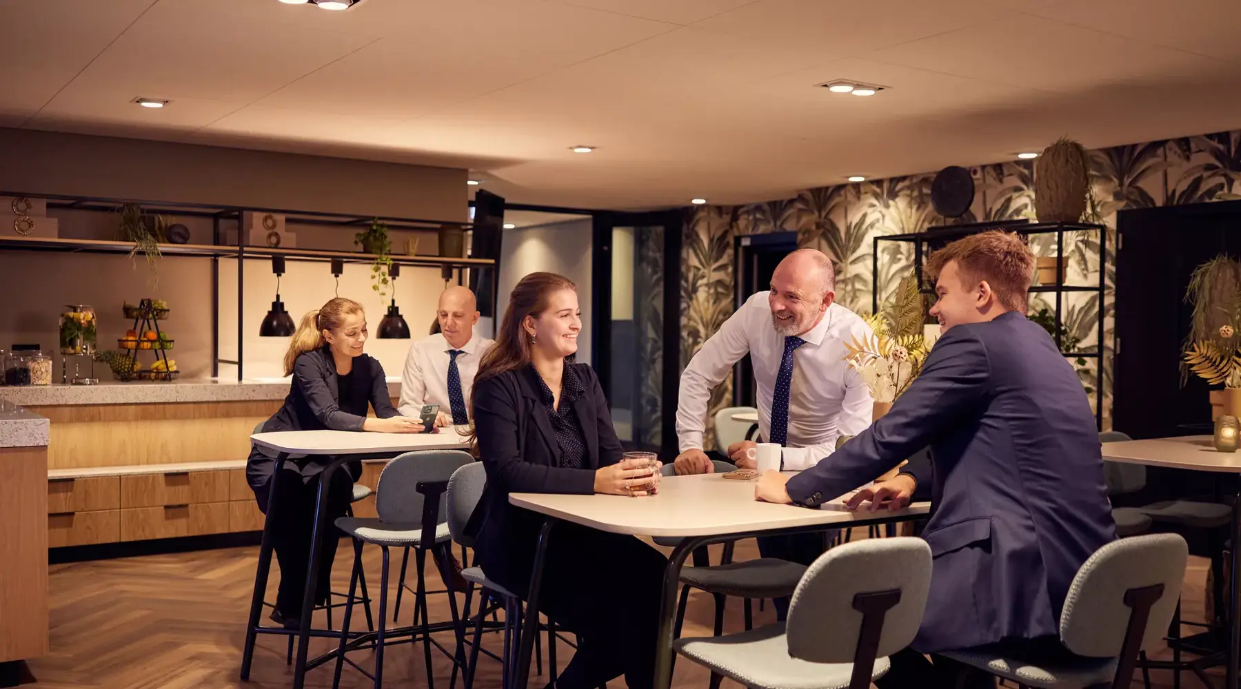 Meerdere mensen hebben een bespreking in de breakout ruimte van een business center van een hotel en genieten ondertussen van een warme drank.