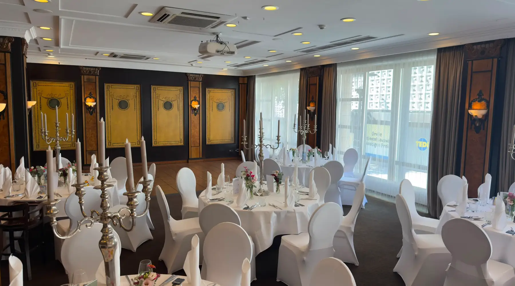 Feestelijk ingerichte evenementenruimte Wollenweber 1, afgescheiden van de aangrenzende ruimte Wollenweber 2, met ronde tafels en witte stoelhoezen in het Van der Valk Hotel Hildesheim.