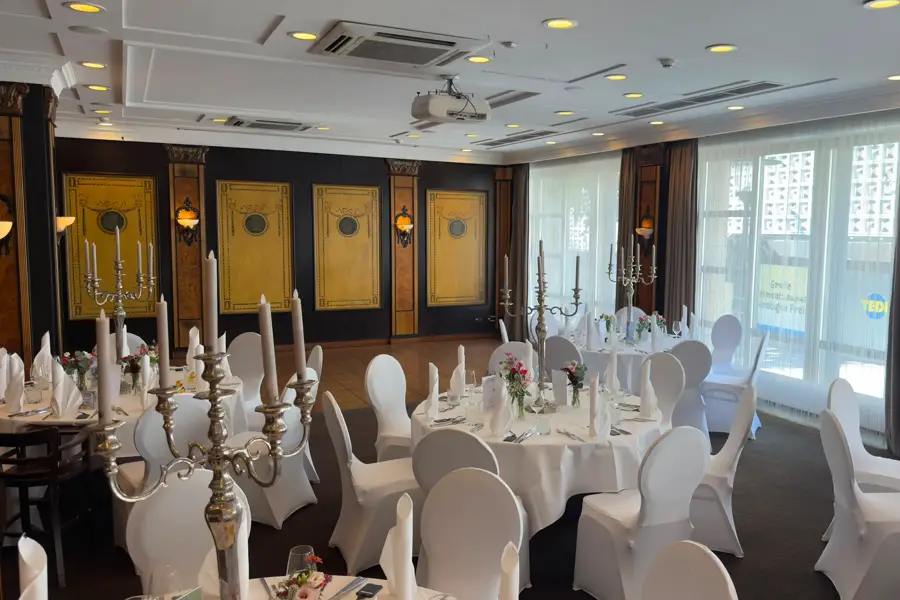 Festively prepared event room Wollenweber 1, separated from the adjacent room Wollenweber 2, with round tables and white chair covers in the Van der Valk Hotel Hildesheim.