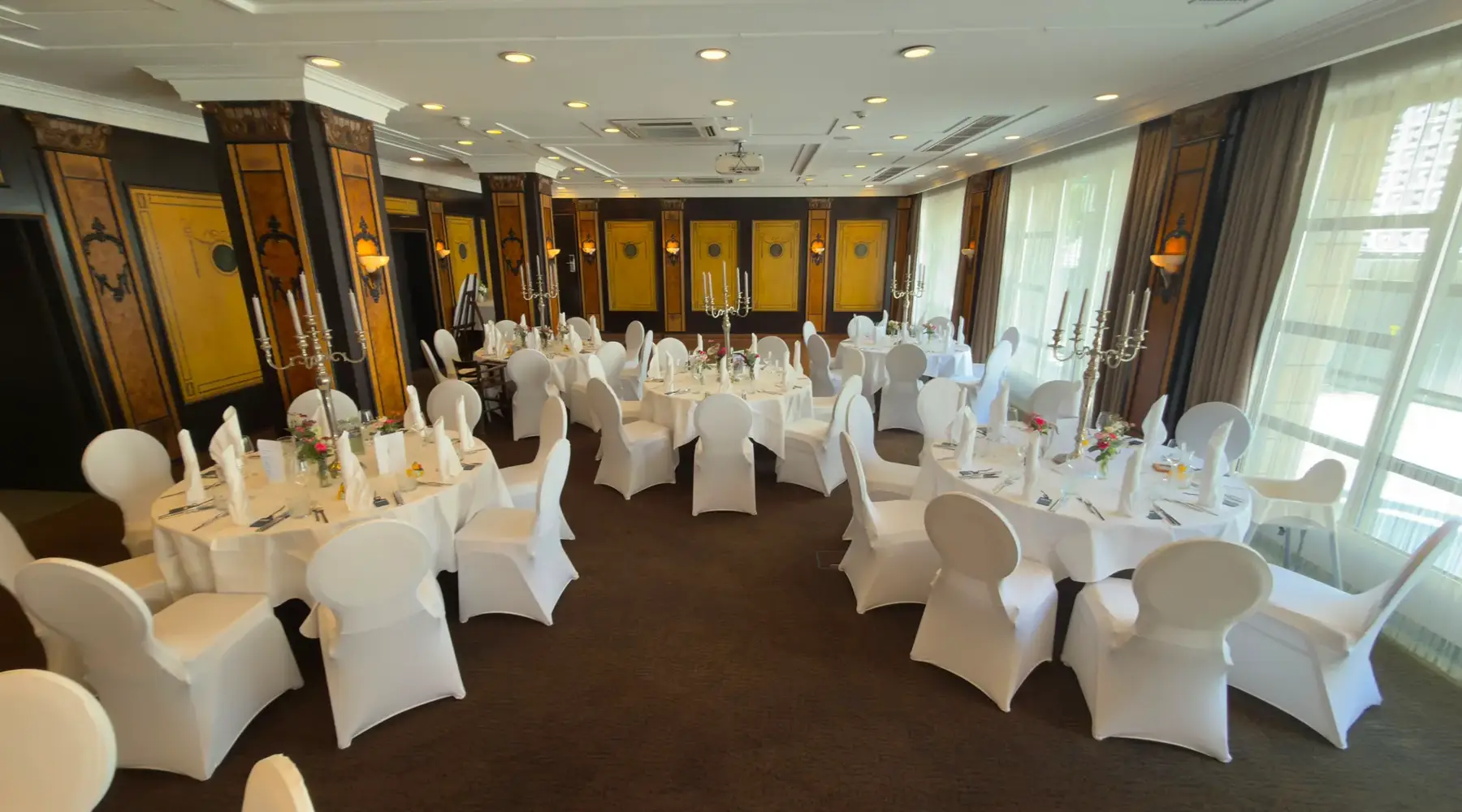 Feestelijk ingerichte evenementenruimte Wollenweber 1, afgescheiden van de aangrenzende ruimte Wollenweber 2, met ronde tafels en witte stoelhoezen in het Van der Valk Hotel Hildesheim.
