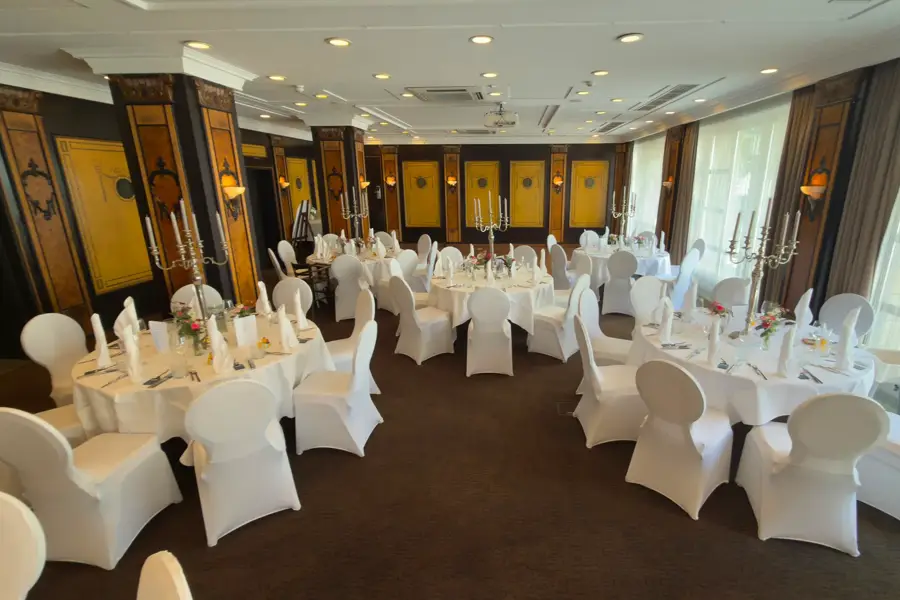 Festively prepared event room Wollenweber 1, separated from the adjacent room Wollenweber 2, with round tables and white chair covers in the Van der Valk Hotel Hildesheim.
