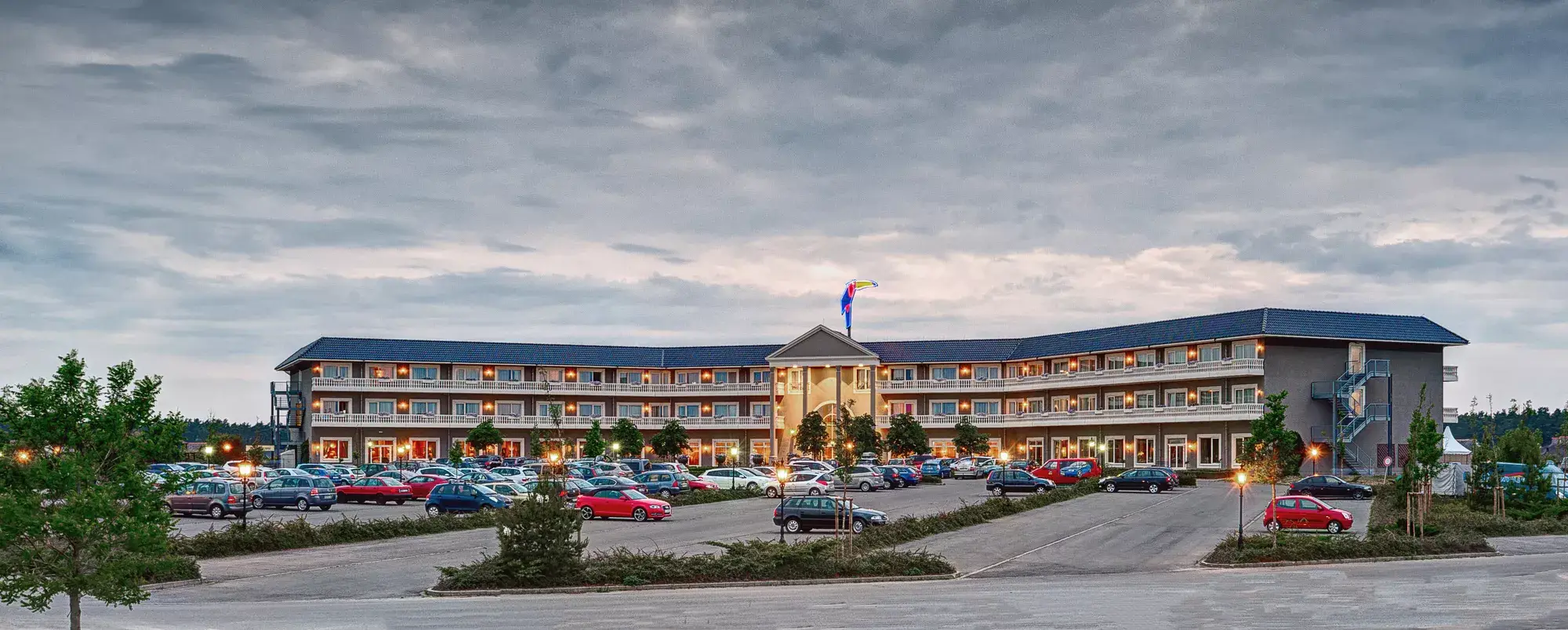Die Vorderseite des Van der Valk Resort Linstow am Abend, stimmungsvoll beleuchtet mit Balkonen, Eingang und Parkplatz im Vordergrund.