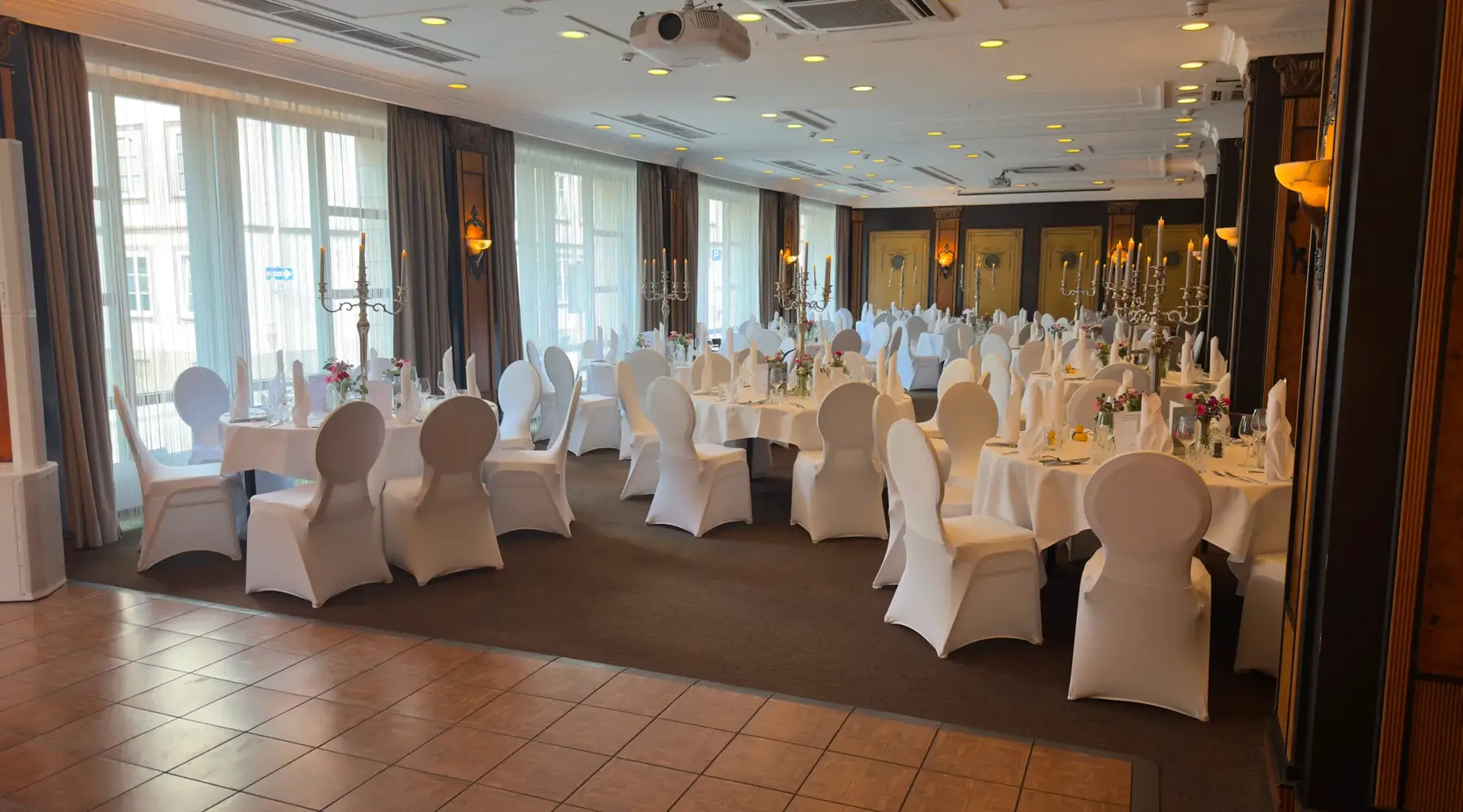 Feestelijk versierde evenementenruimte met ronde tafels en een dansvloer op de voorgrond die indien nodig gebruikt kan worden, in het Van der Valk Hotel Hildesheim.