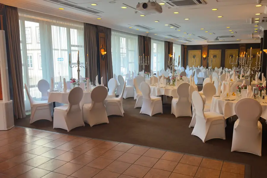 Festively decorated event room with round tables and a dance floor in the foreground that can be used if needed, in the Van der Valk Hotel Hildesheim.